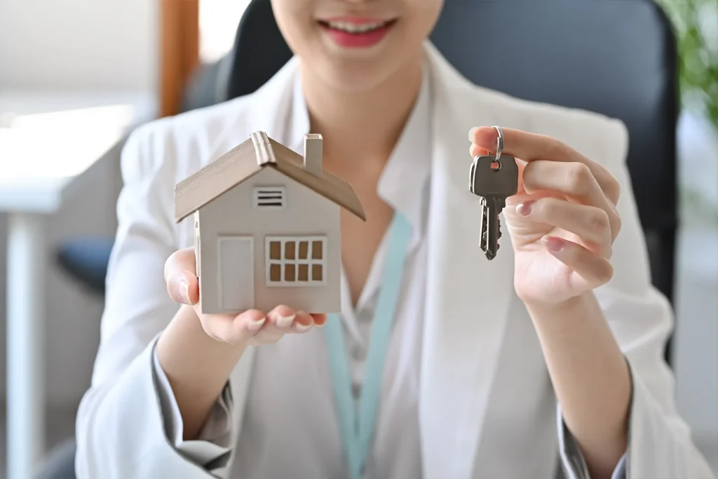 An estate agent holds a model house in one hand and a door key in the other